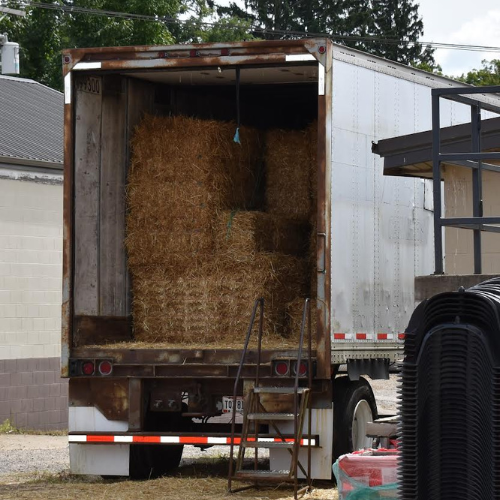 A box truck full of hay bales parked outside of Village Hardware & Rental.