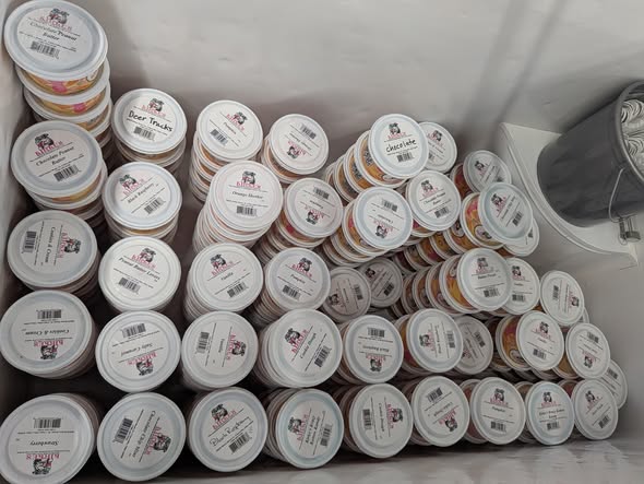 Numerous stacked ice cream tubs with white lids and labels fill a freezer. The setup suggests abundance and variety, conveying freshness and choice.