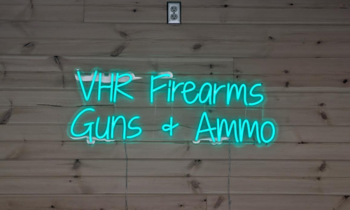 Neon sign on a wooden wall advertising 'VHR Firearms Guns & Ammo'.