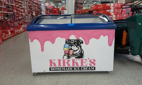 Ice cream freezer in a store, featuring "Kirke's Homemade Ice Cream" with a cartoon bulldog licking a cone. Pink drips decorate the top.